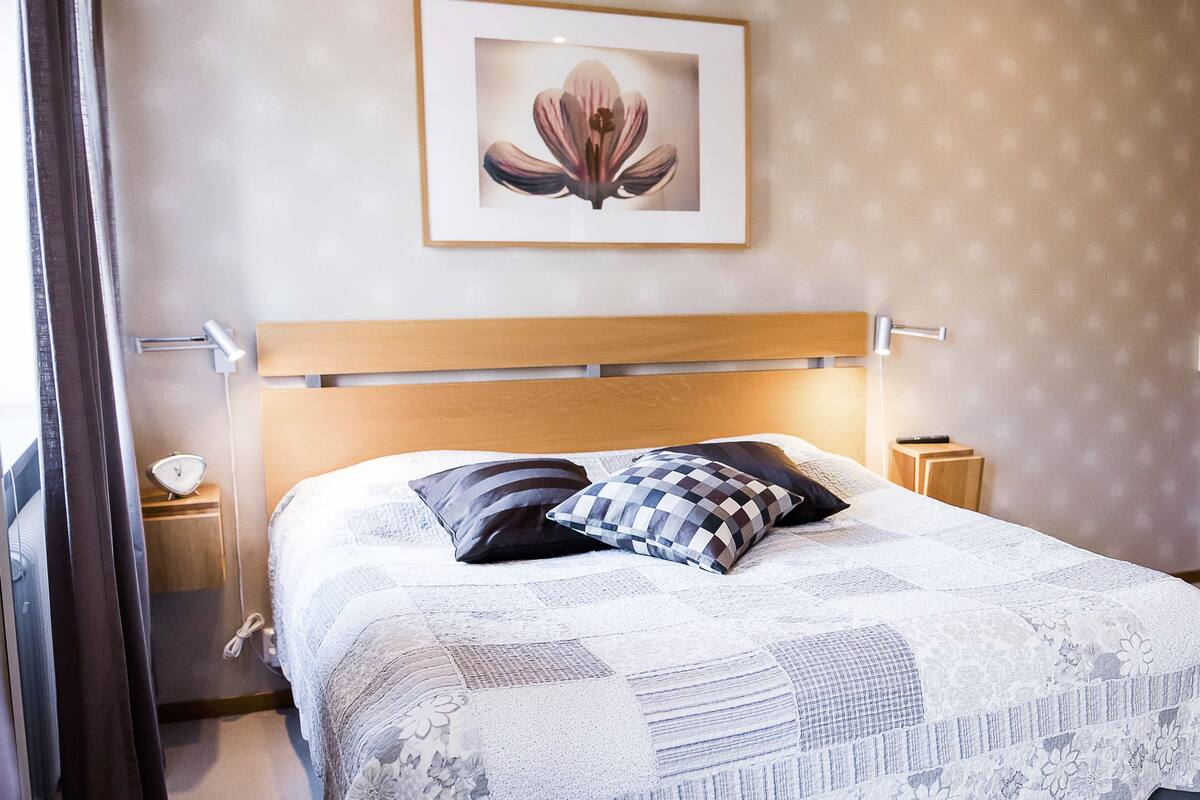 A neatly made bed with a checkered pillow and a floral wall art piece above it.