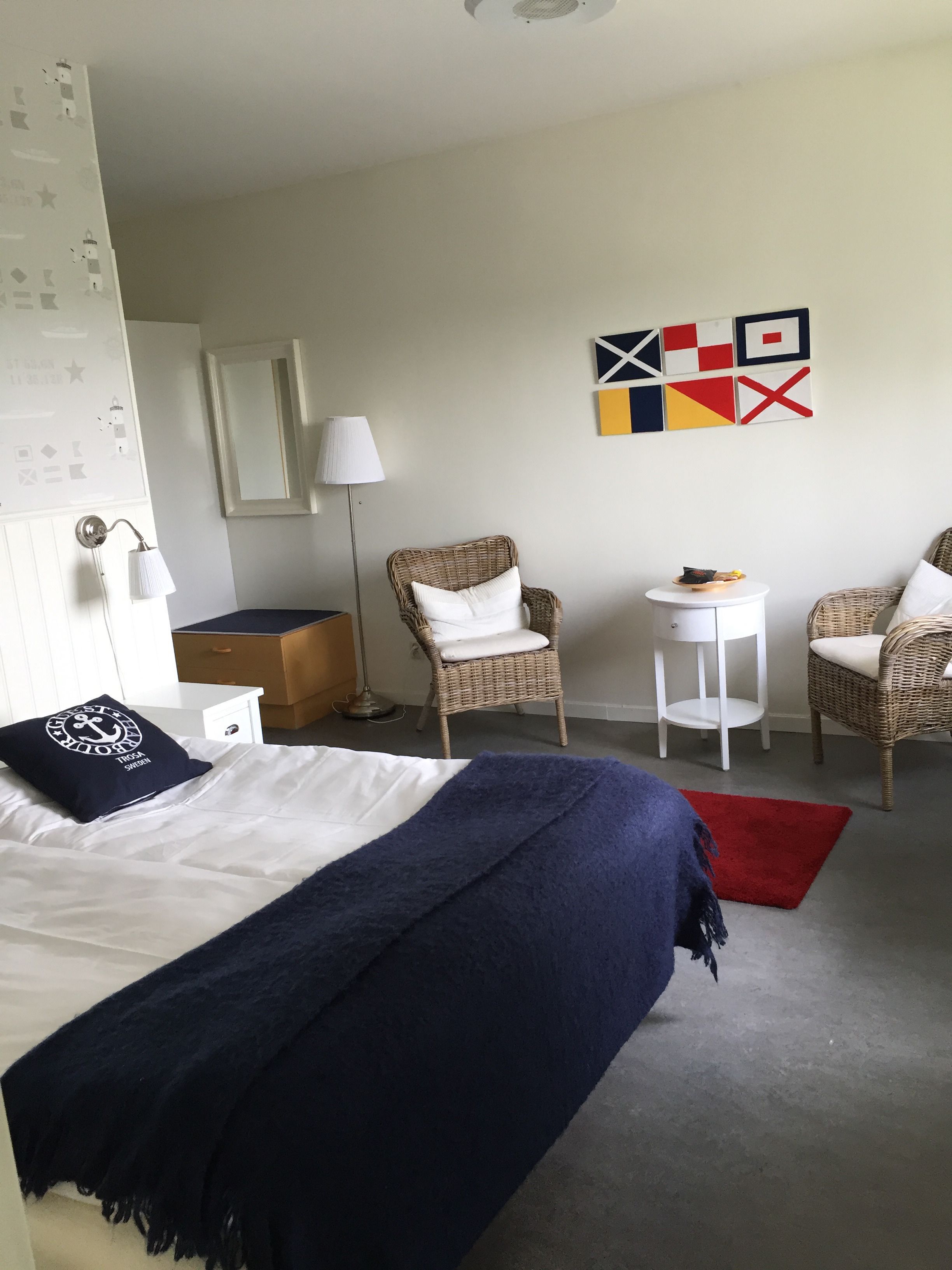 Hotelkamer met een bed, twee rieten stoelen, een klein tafeltje, een lamp en een muur met abstracte kunst.