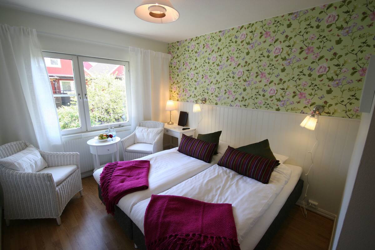 A hotel room with two beds, a chair, a small table, and a window with curtains.