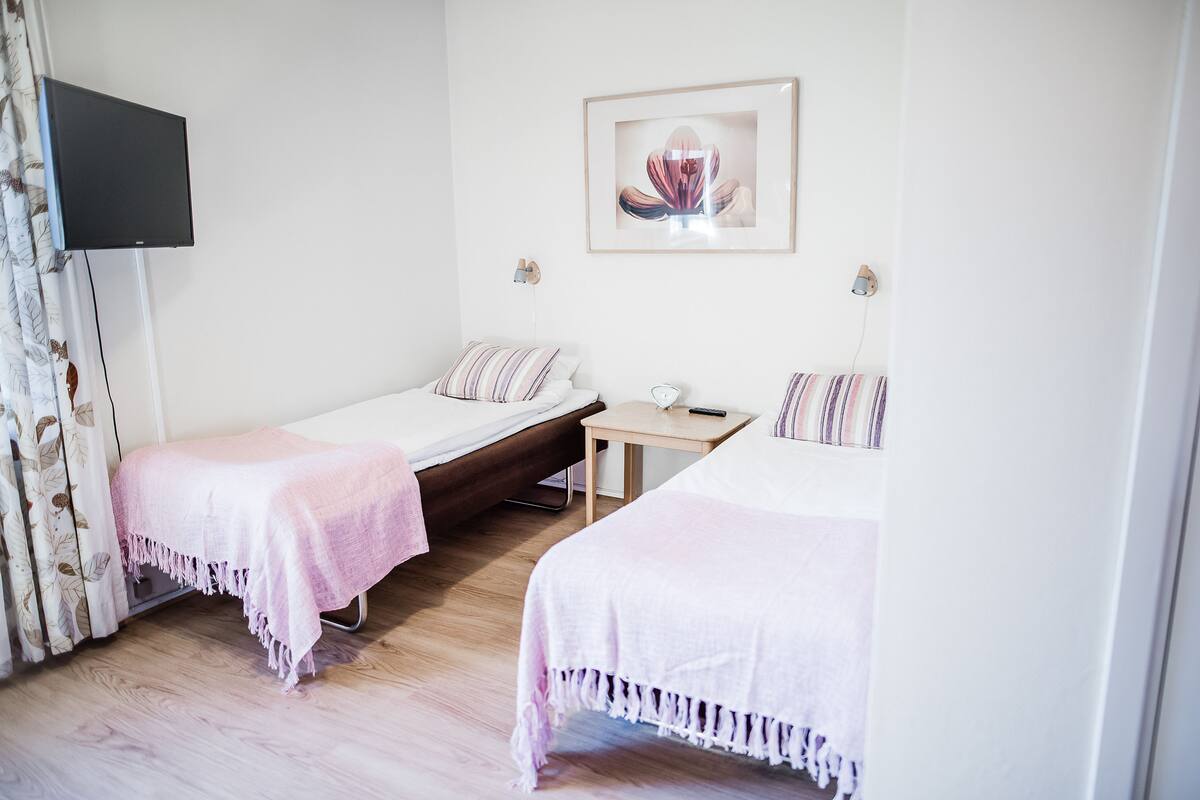 A bedroom with two single beds, a small table, a TV mounted on the wall, and a framed picture above the bed.