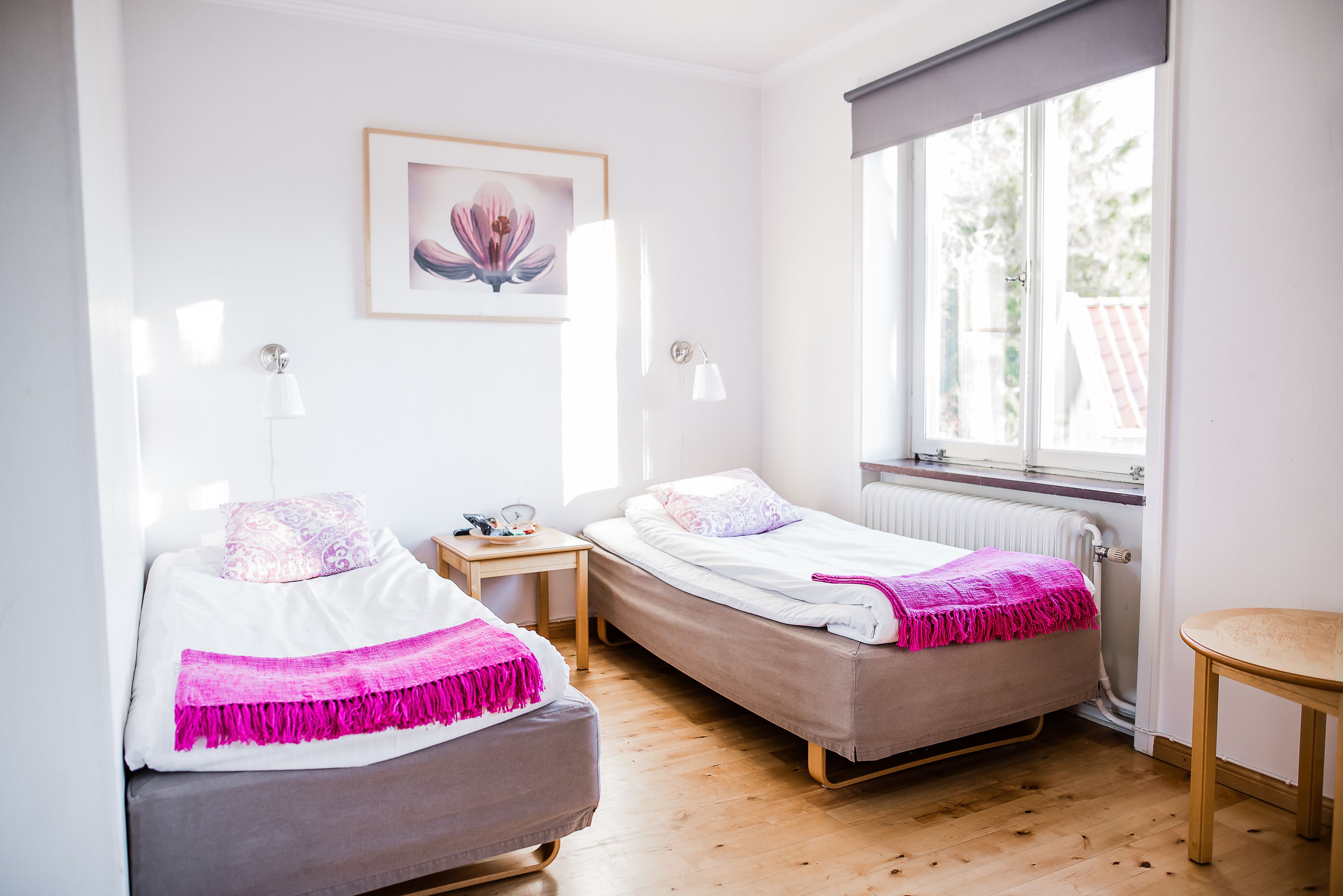 Une chambre avec deux lits simples, un plancher en bois, une fenêtre avec vue et une petite table avec une lampe.
