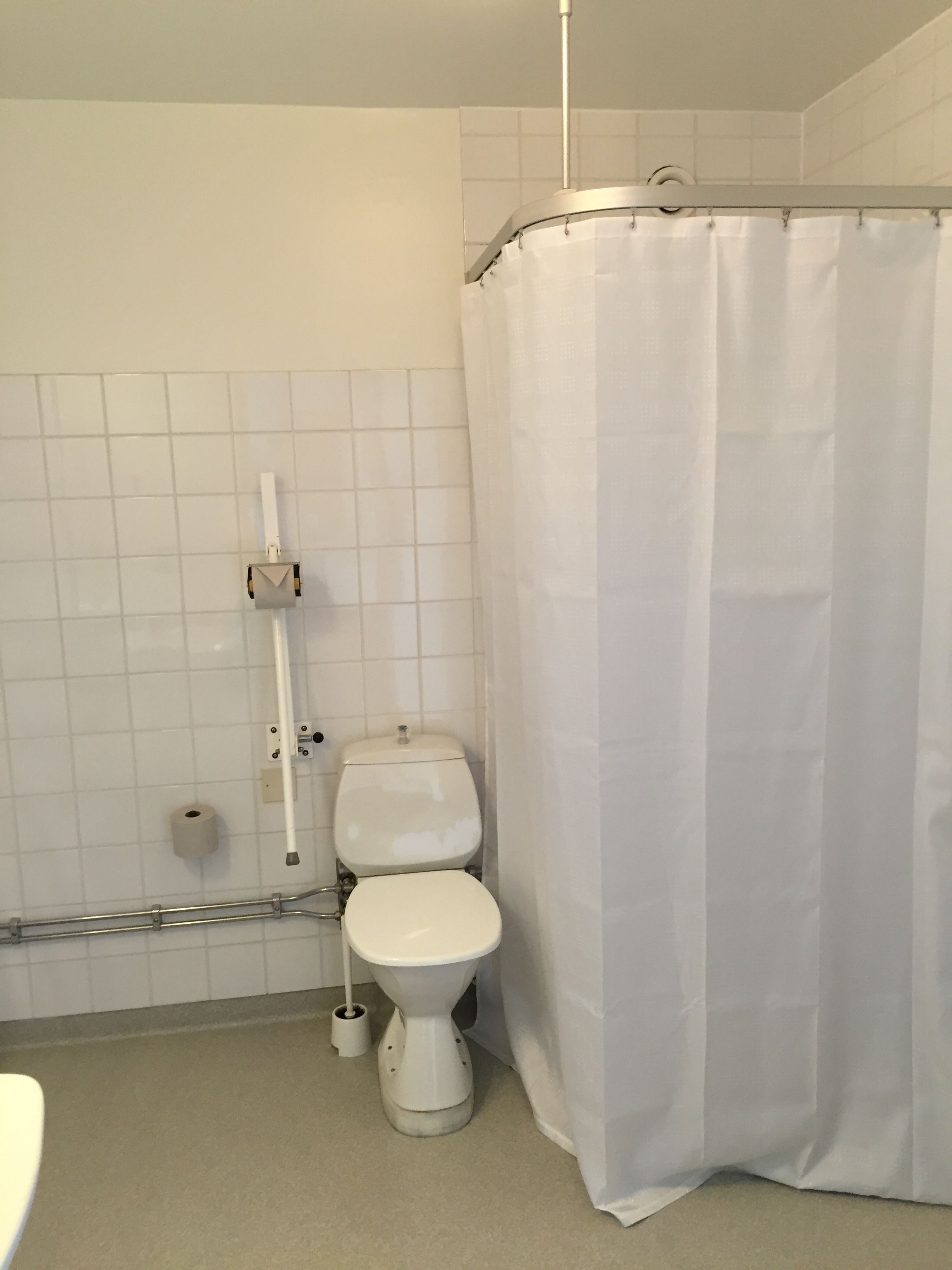 Un baño con inodoro, cortina de ducha y barra de apoyo.