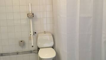 Un baño con inodoro, cortina de ducha y barra de apoyo.