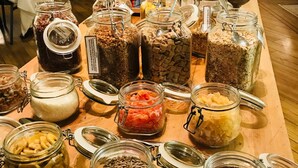 Una mesa de buffet con diversos alimentos en frascos de vidrio, incluyendo opciones identificadas como plátanos y semillas de girasol.