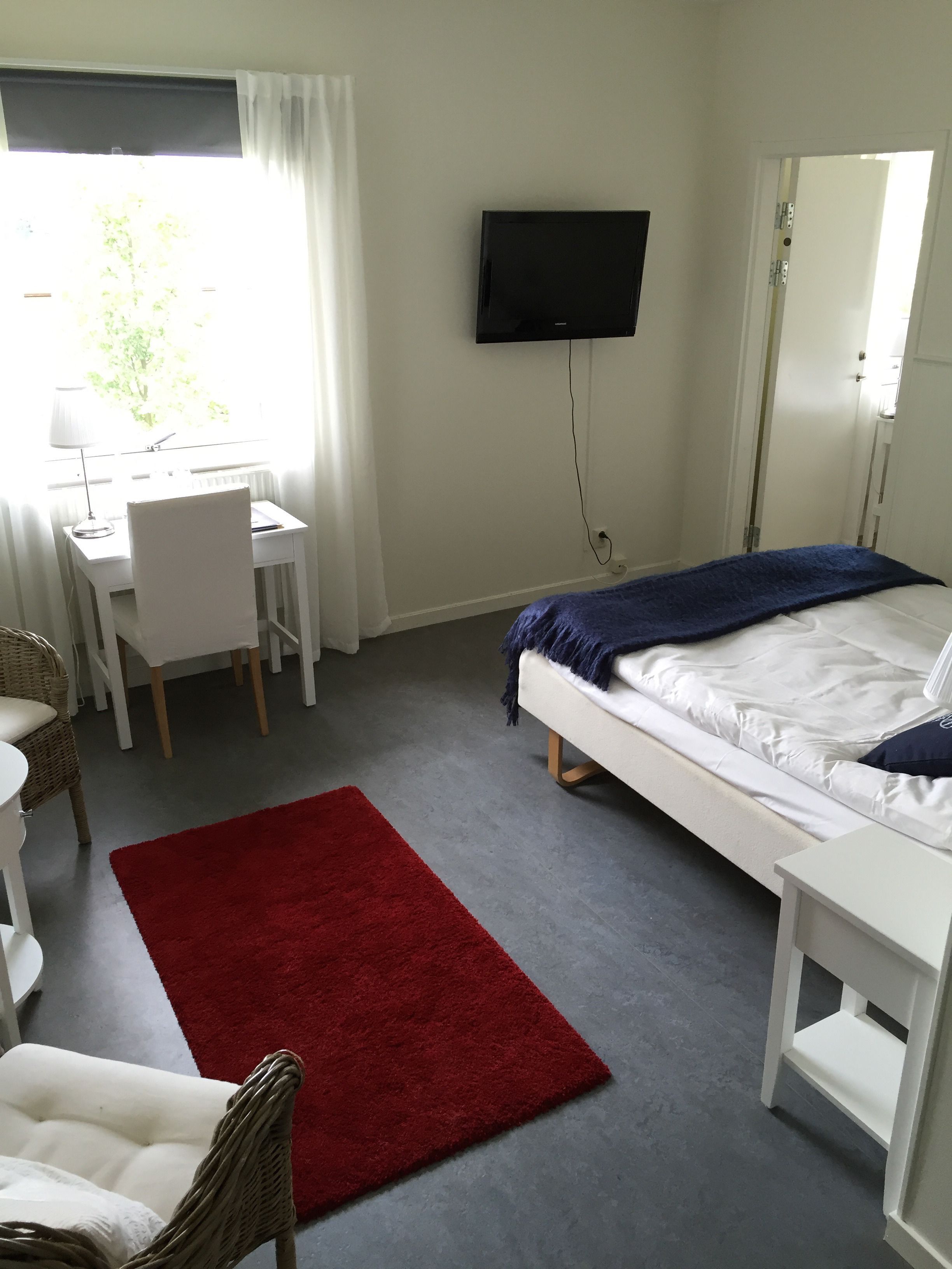 A hotel room with a bed, a desk, a chair, a television, and a red rug.