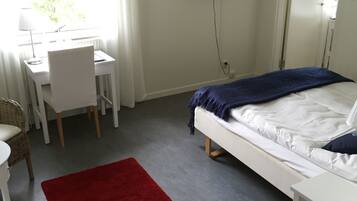 A hotel room with a bed, a desk, a chair, a television, and a red rug.