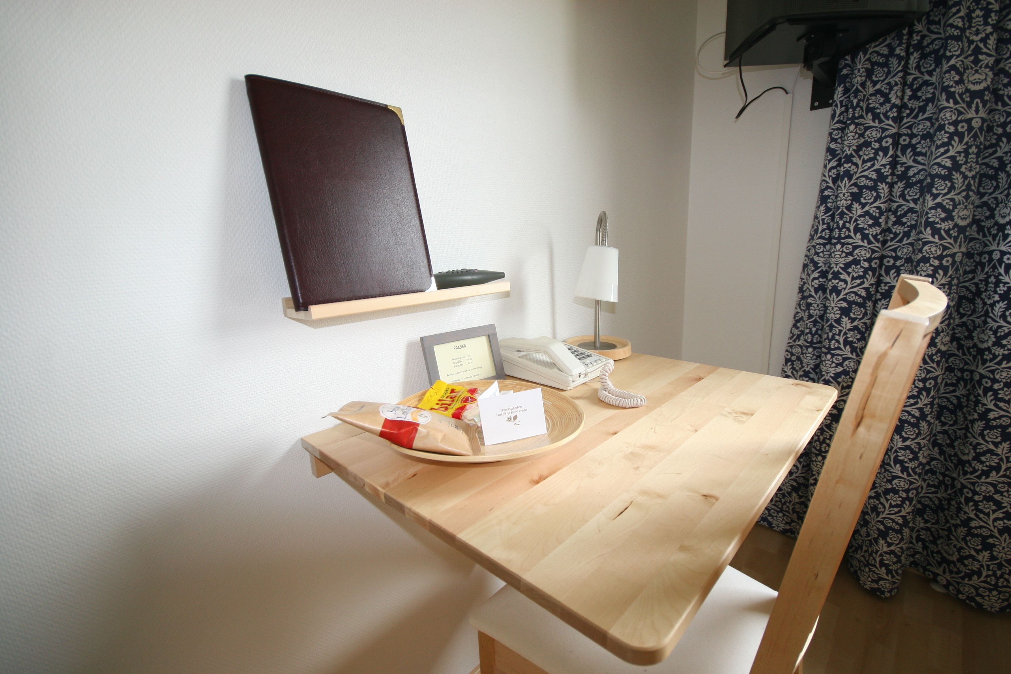 Una mesa de madera con un teléfono, una bandeja con aperitivos, un menú y un estante en la pared con un objeto negro.