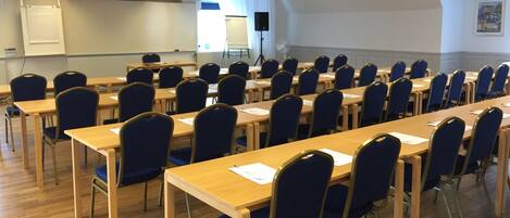 A conference room with rows of tables and chairs, a projector, and a whiteboard.