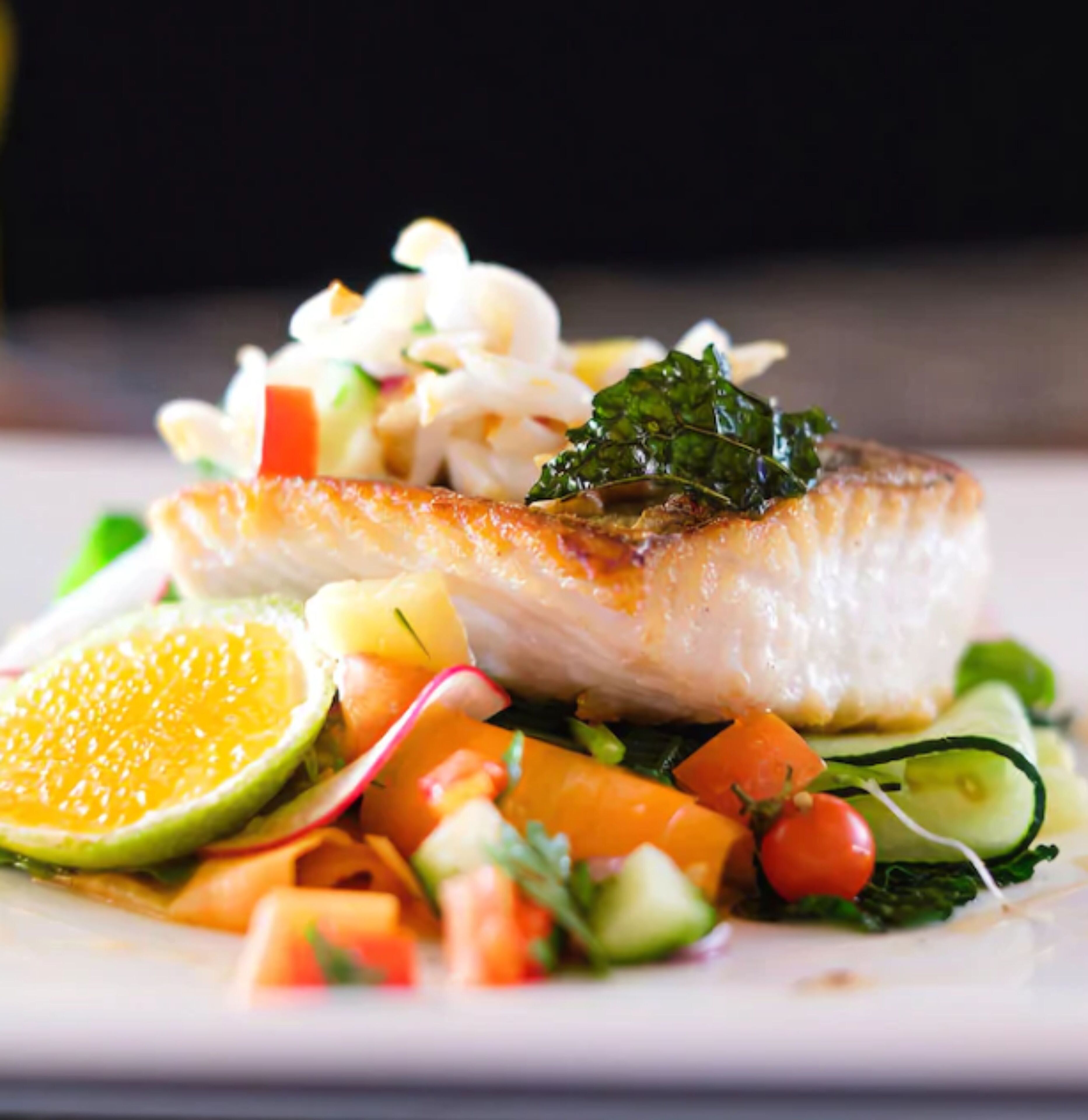 A plate with a piece of fish, vegetables, and a citrus slice.