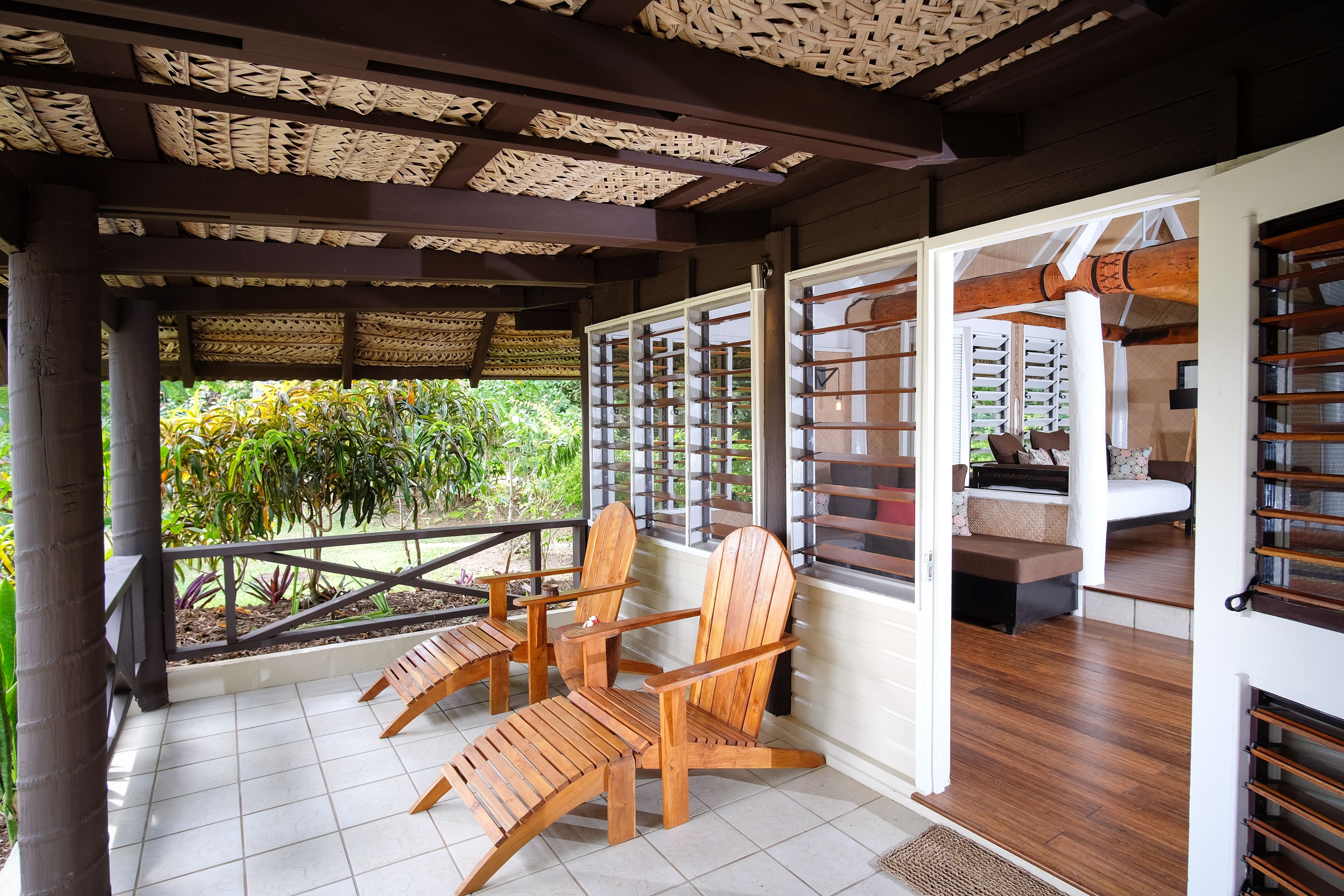 A covered outdoor seating area with wooden chairs and a view of a garden.