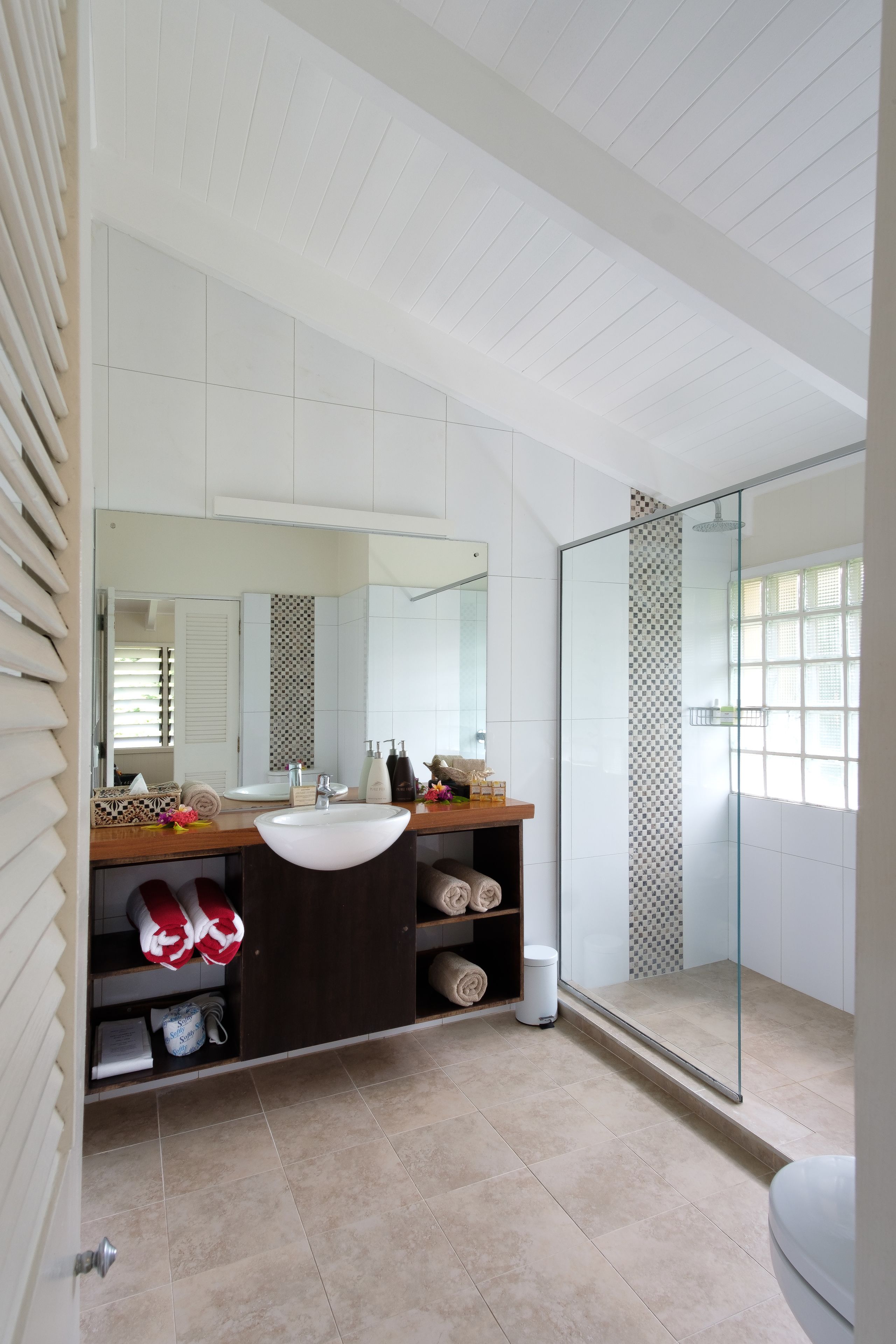 Un baño moderno con un espejo grande, lavamanos blanco y cabina de ducha de vidrio.