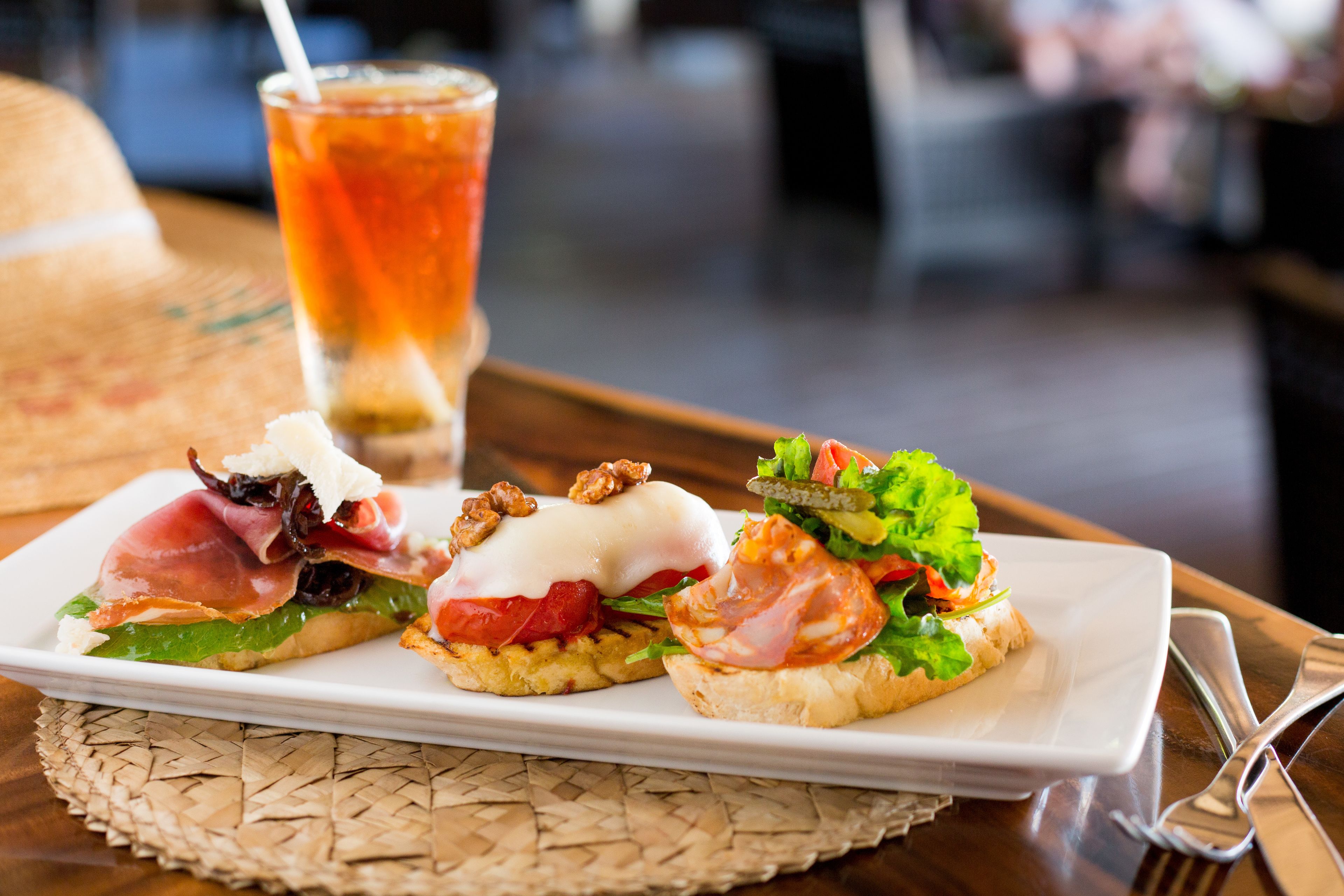 A plate of appetizers on a woven placemat, a glass of iced tea, and a fork and knife on a wooden table.