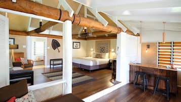 Una habitación amplia con una cama grande, techo de madera, una zona de cocina con taburetes y un rincón de descanso con sofá.