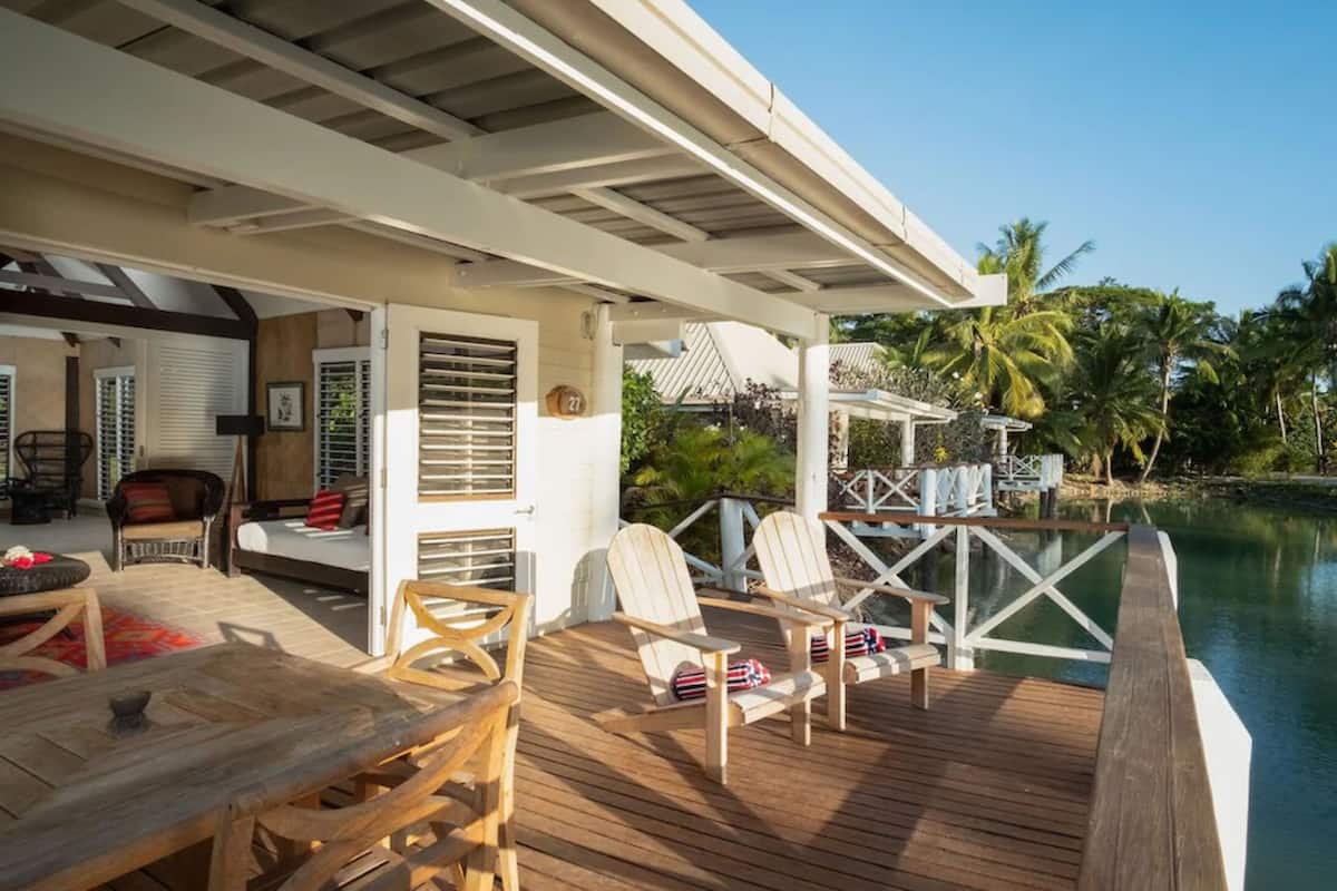 Une terrasse en bois avec des sièges d’extérieur, une piscine et un espace abrité offrant une vue sur les palmiers.