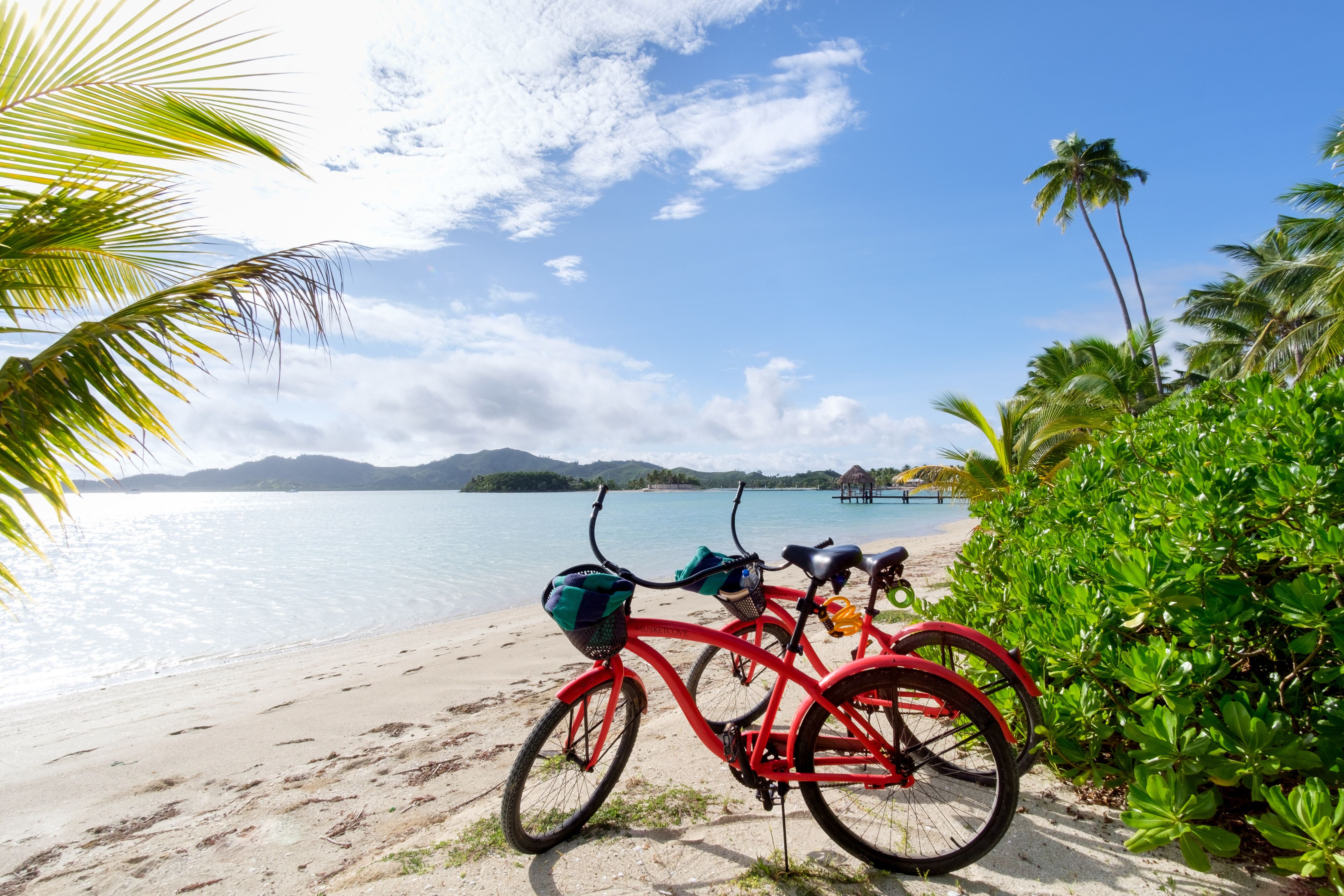 Una playa con una bicicleta roja y una estructura de techo de paja al fondo.