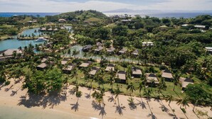 Vista aérea de un resort con varias construcciones tipo bungalow, una playa y una masa de agua.
