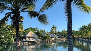 Un resort tropical con una masa de agua, palmeras y bungalows sobre el agua.