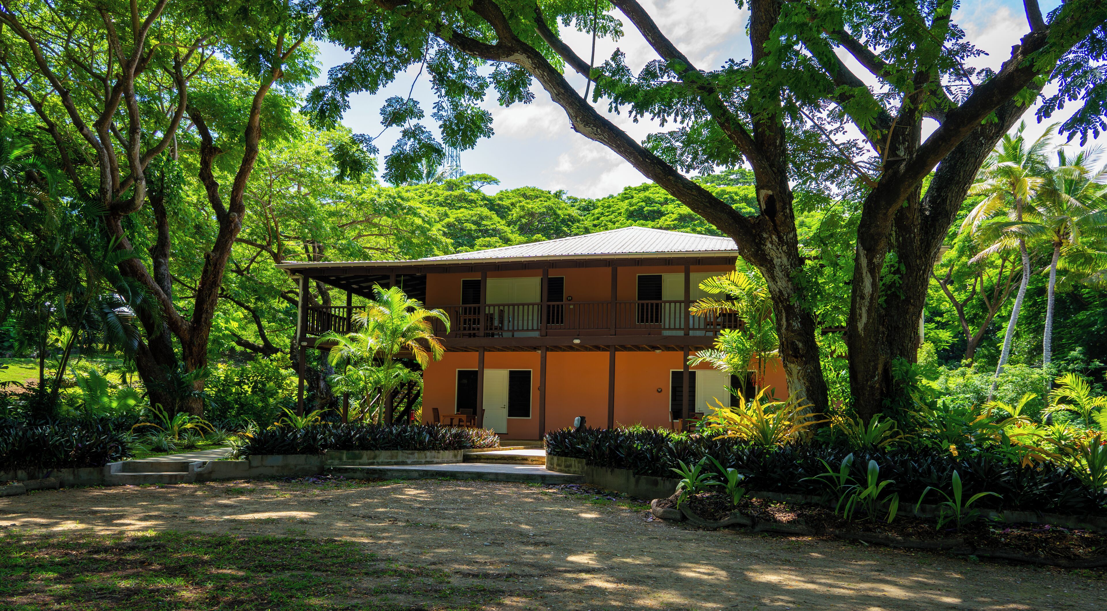 A two-story building with a balcony, surrounded by lush greenery and trees.
