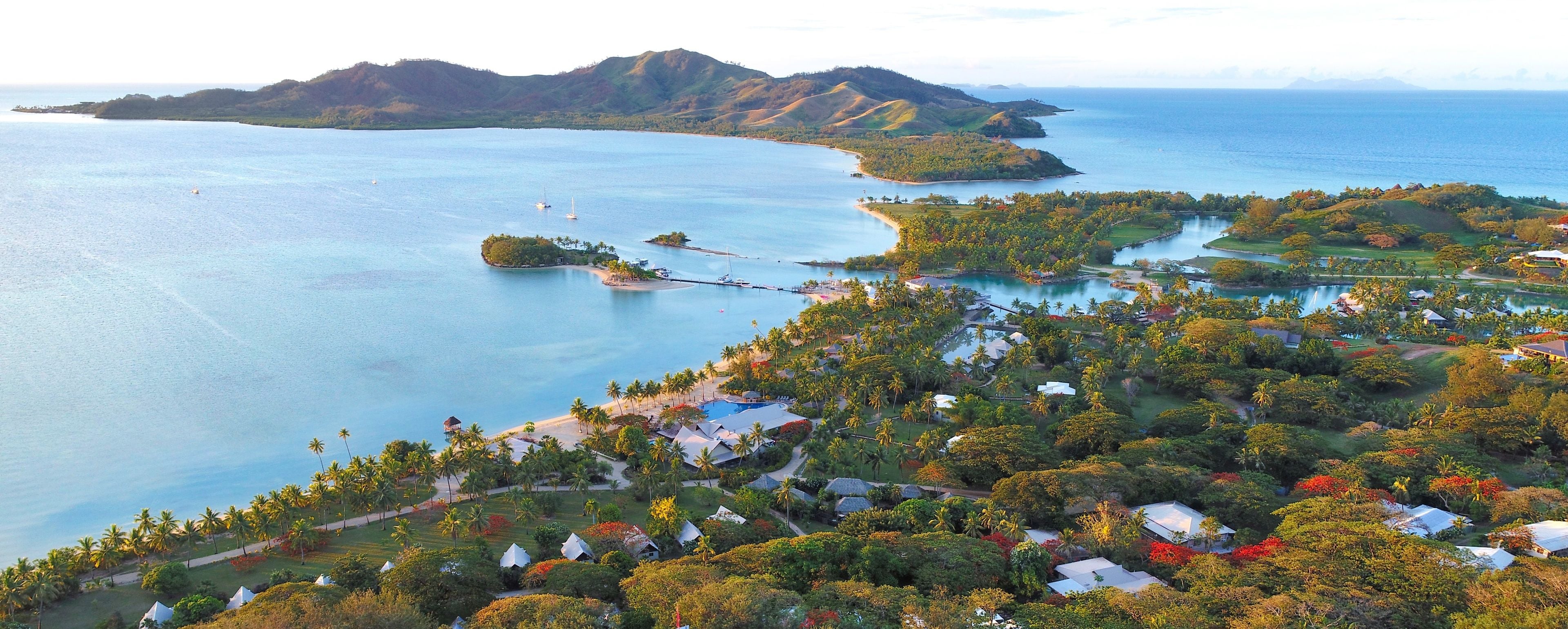 An aerial view of a coastal resort with multiple islands, clear blue waters, and lush greenery.