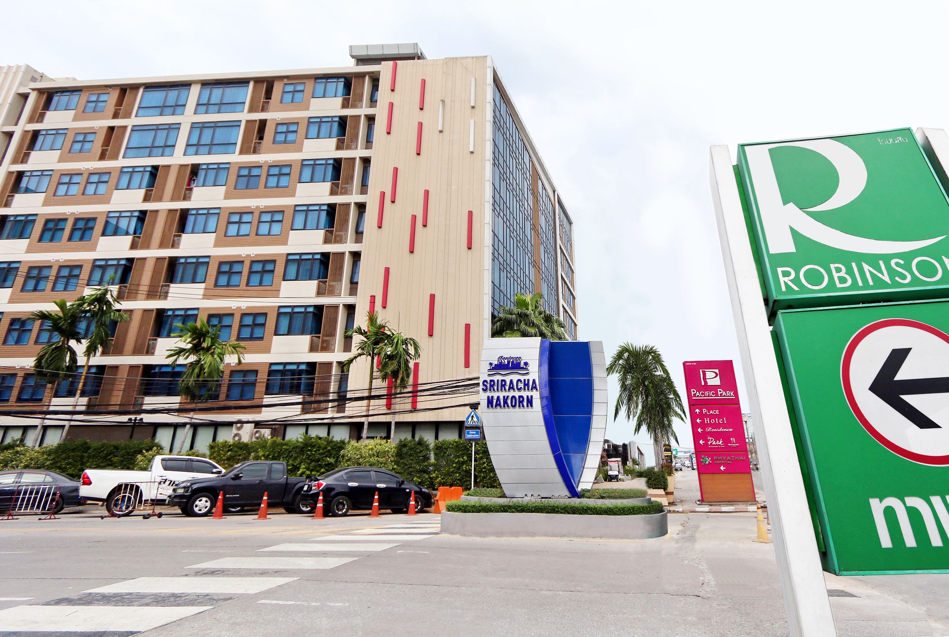 A multi-story hotel with a modern design, featuring a prominent sign for 'Sriracha Nakorn' and a 'Pacific Park' sign.