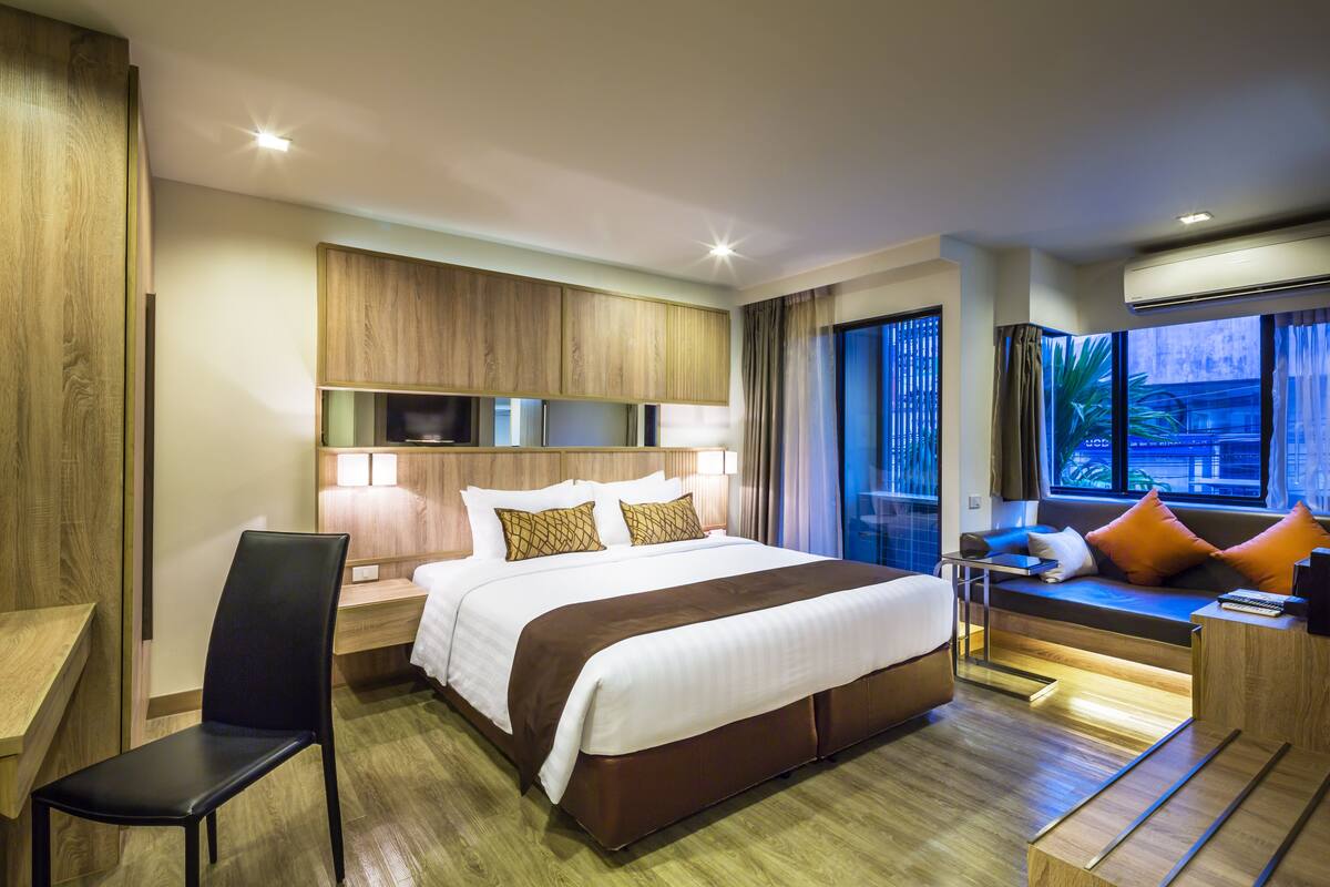 Una habitación de hotel moderna con una cama grande, un escritorio, una silla y una zona de estar junto a la ventana.