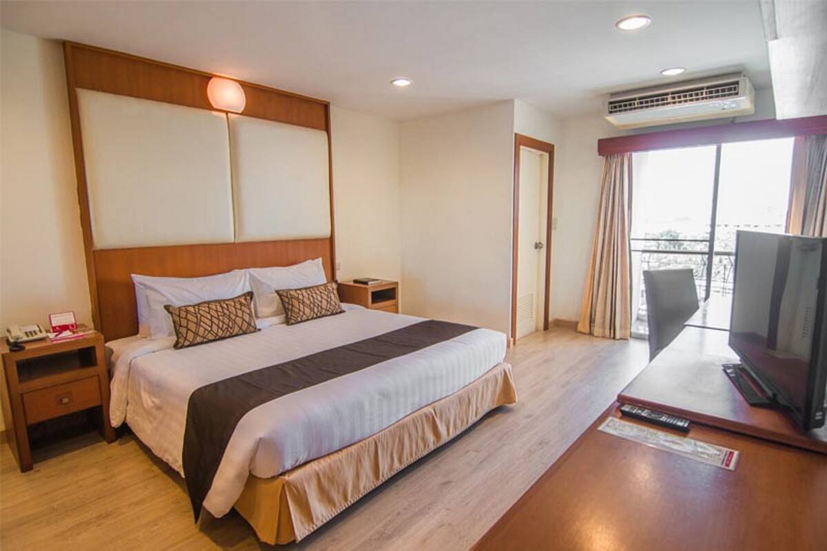 Habitación de hotel con una cama grande, televisión, aire acondicionado y balcón con cortinas.