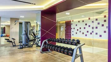 Uma academia com equipamentos de ginástica, um suporte de halteres e um espelho grande na parede.
