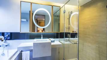 Un baño moderno con cabina de ducha de vidrio, un espejo grande con luz circular y un lavabo blanco.