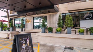 Un edificio moderno con un área de estar al aire libre techada, plantas en macetas y un cartel.
