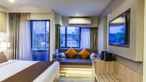 Habitación de hotel con una cama grande, una zona de estar con cojines, televisión y vistas al exterior.