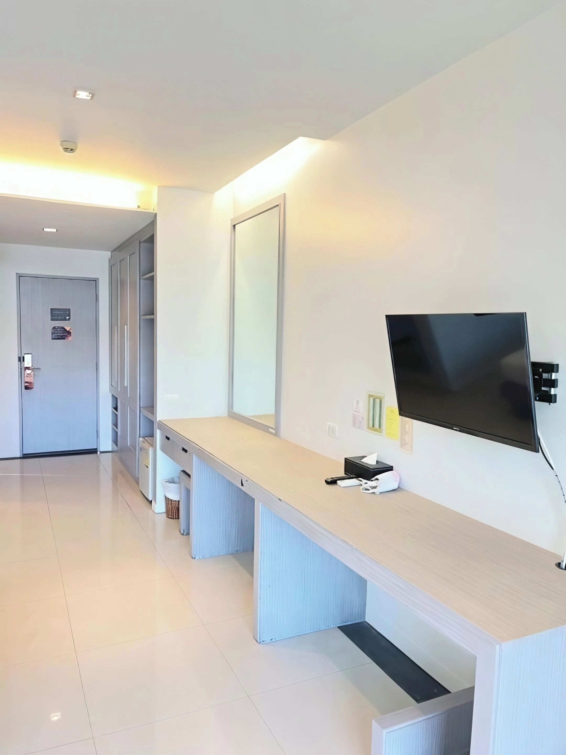 A modern hotel reception area with a long reception desk, a large mirror, and a flat-screen TV.