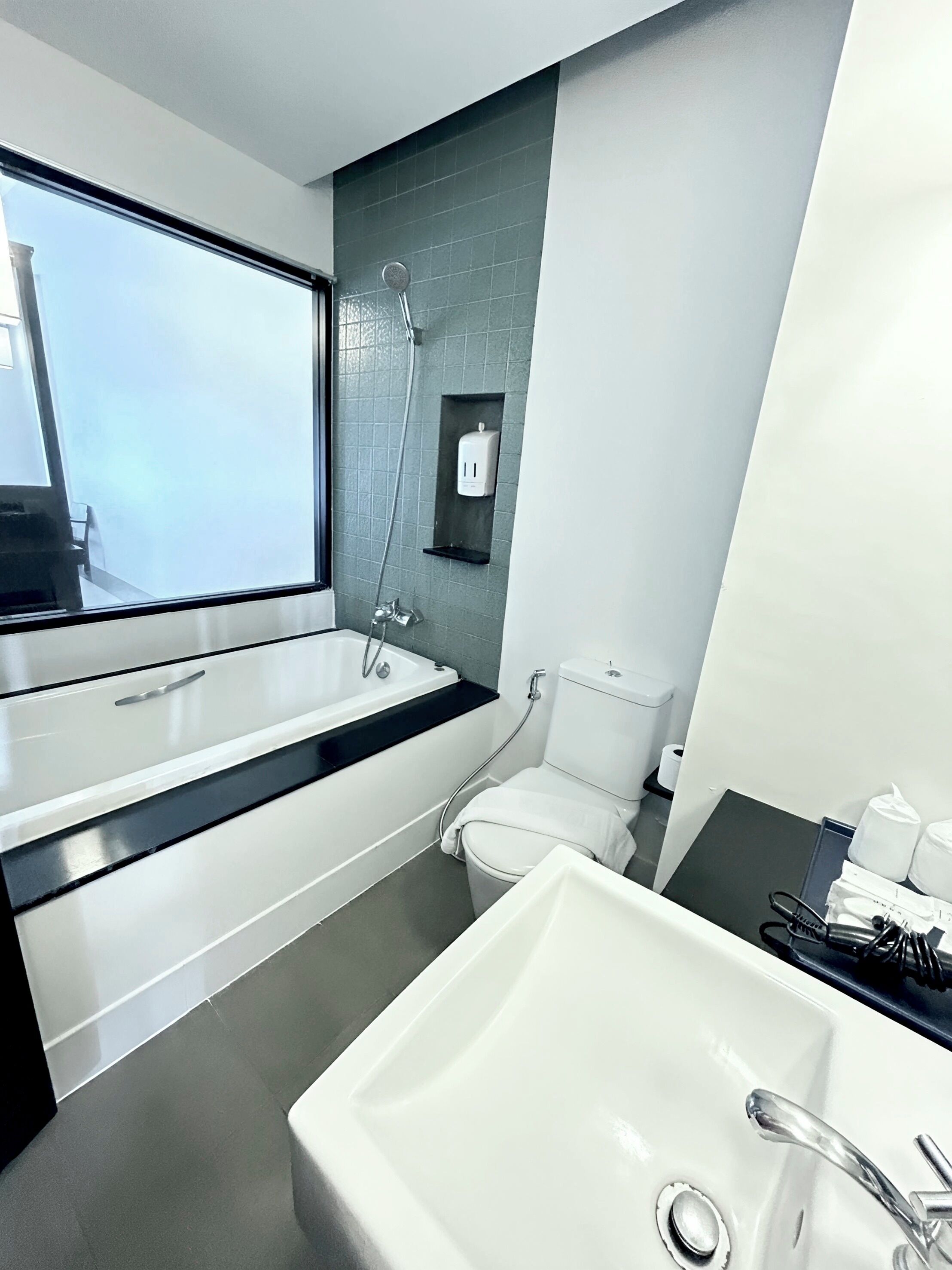 A modern bathroom with a large window, a bathtub, a toilet, and a sink.