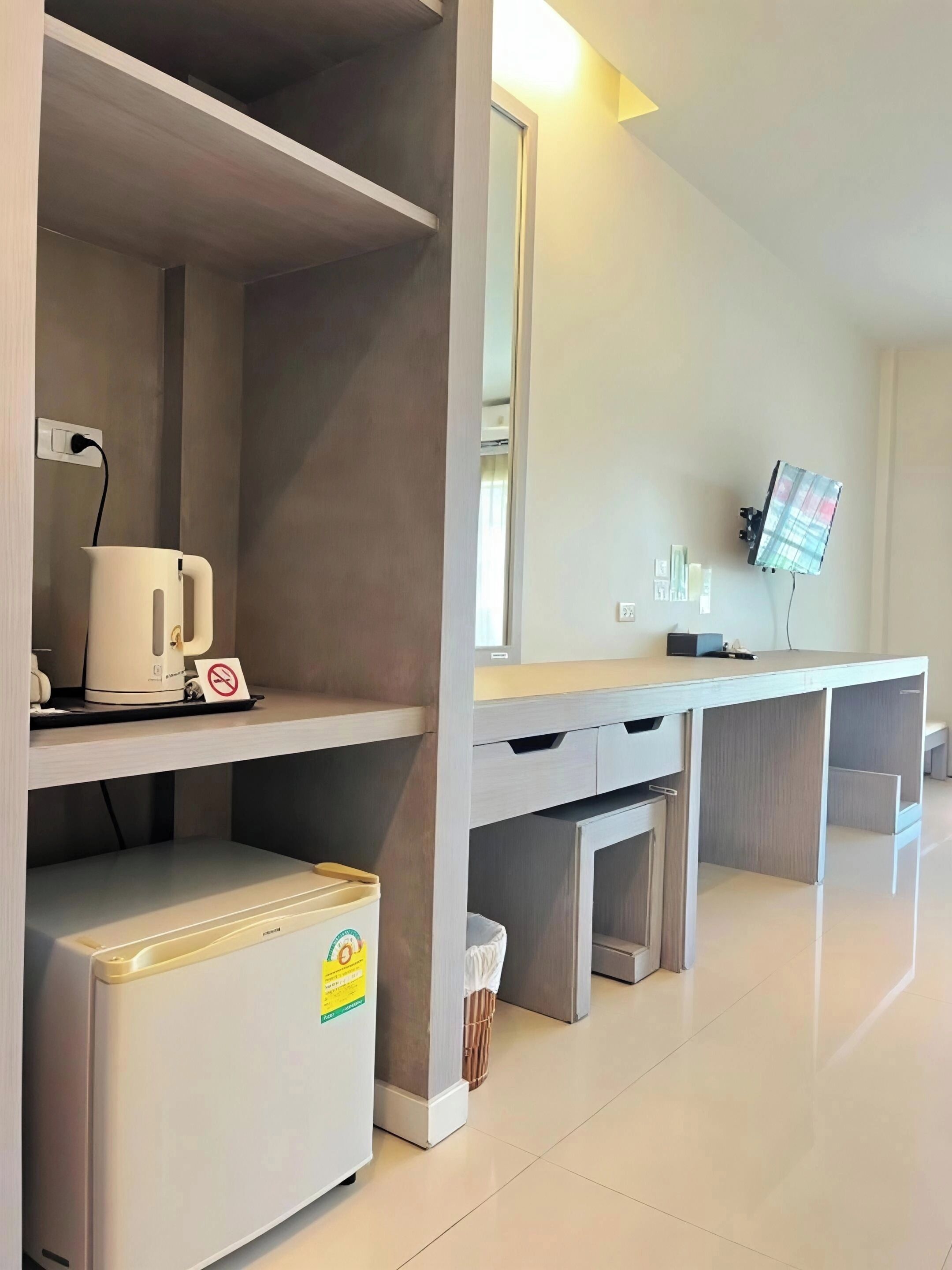 A modern hotel room with a kitchenette, a flat-screen TV mounted on the wall, and a clean, minimalist design.