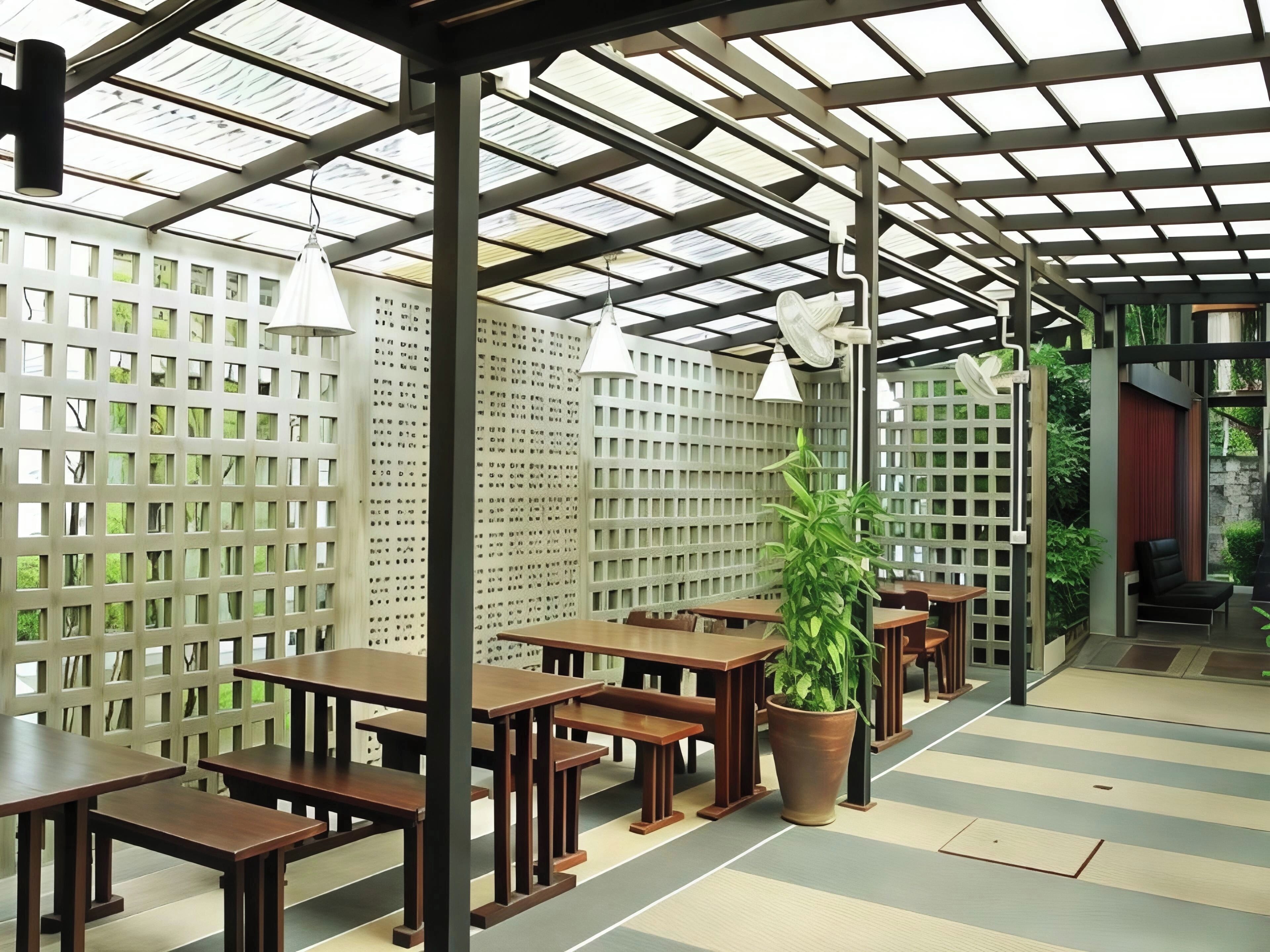 An indoor patio area with wooden tables and benches, a large potted plant, and a ceiling with skylights.