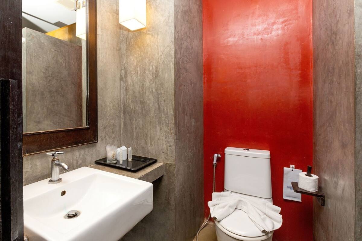 Un baño con lavabo blanco, espejo, inodoro y pared decorativa roja.