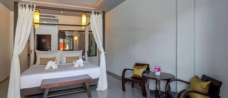 A four-poster bed with a canopy, a ceiling fan, a bedside table, a chair, and a small round table with a vase of flowers.