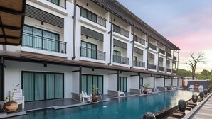 A modern hotel with a long swimming pool, multiple balconies, and a view of the surrounding landscape. - Phuketa Hotel Phuket Town (Ratsada)