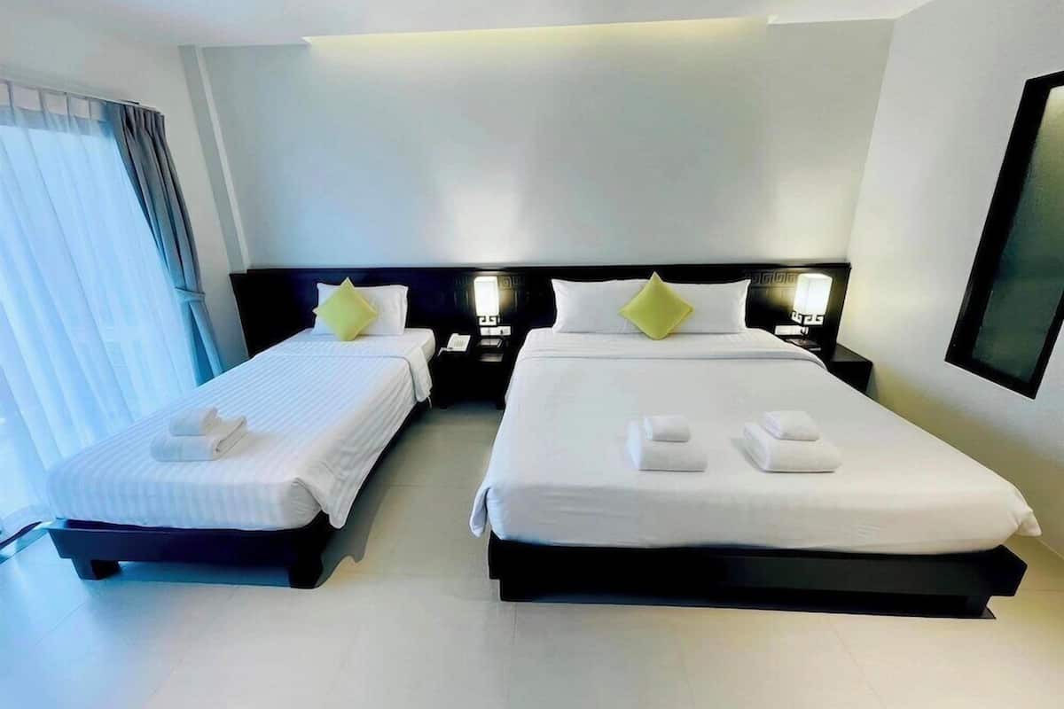 Habitación de hotel con dos camas, un ventanal con cortinas y una mesita de noche con lámpara.