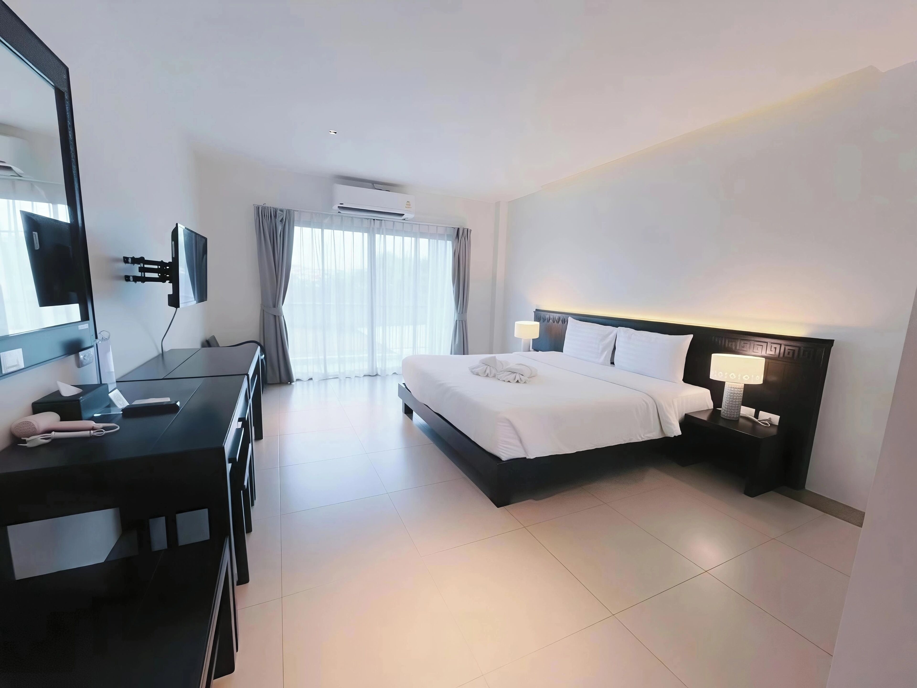 A hotel room with a bed, a desk, a chair, a TV, and a window with curtains.