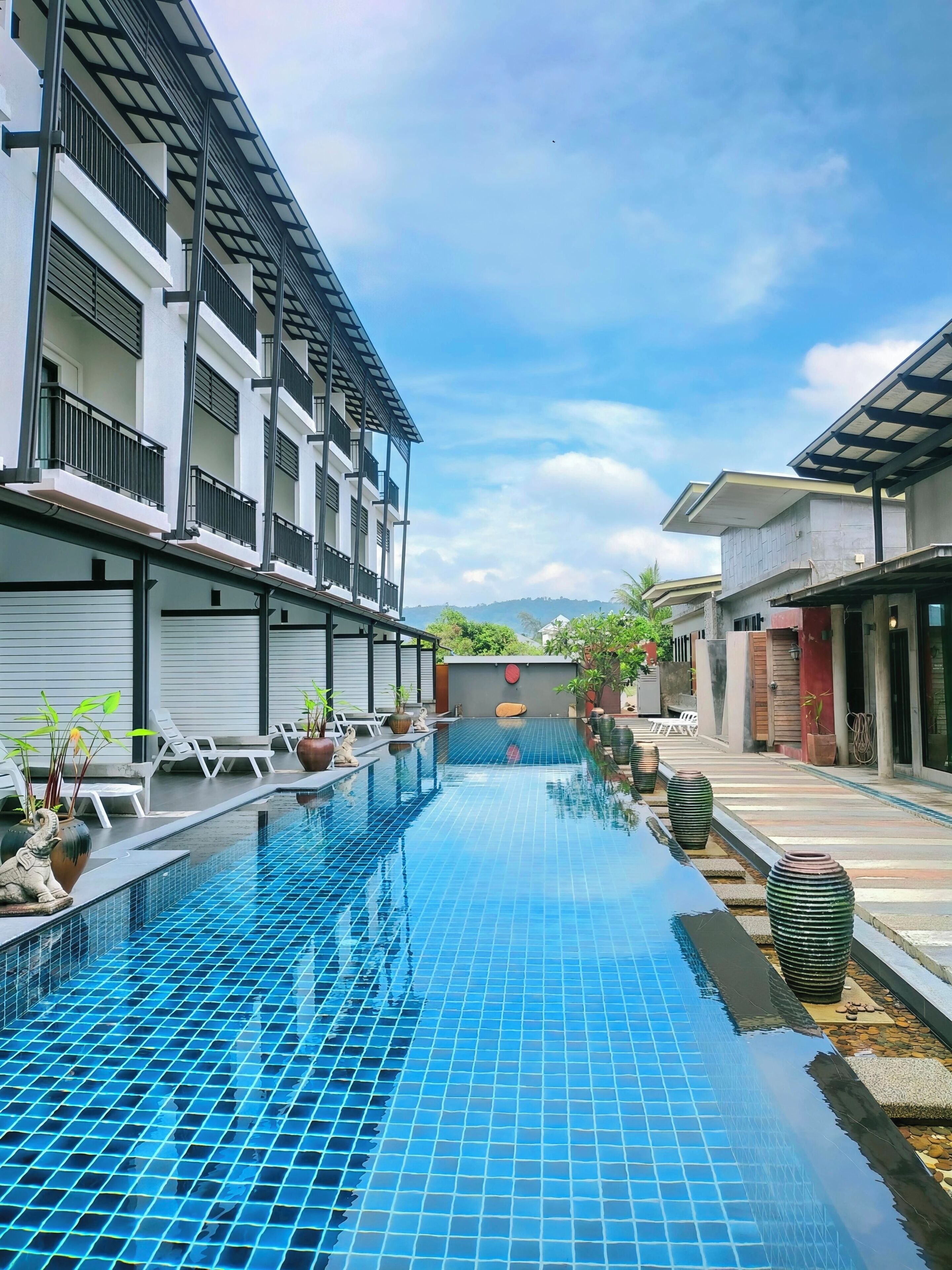 A swimming pool with tiled flooring, lounge chairs, and potted plants.