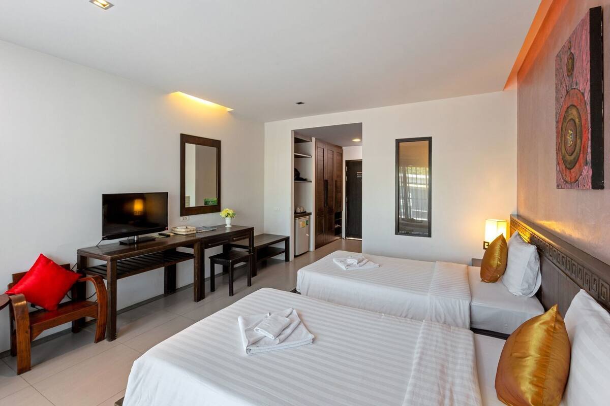 Una habitación de hotel con dos camas, un escritorio con televisor, una silla y un armario.