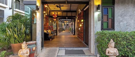 A corridor with a wooden floor leading to a room with a bed and a bench.