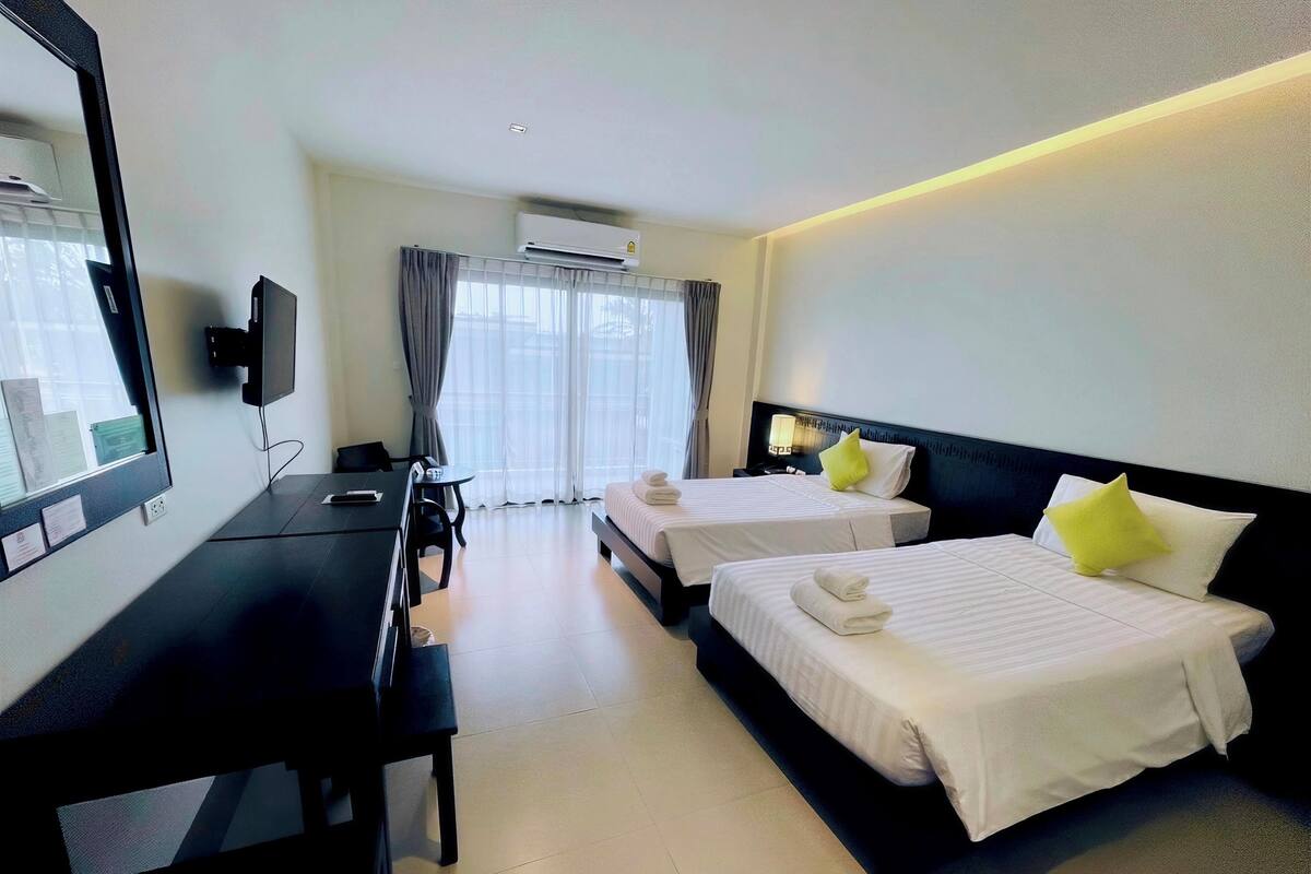 Habitación de hotel con dos camas, un escritorio, una silla, un televisor y un aire acondicionado.