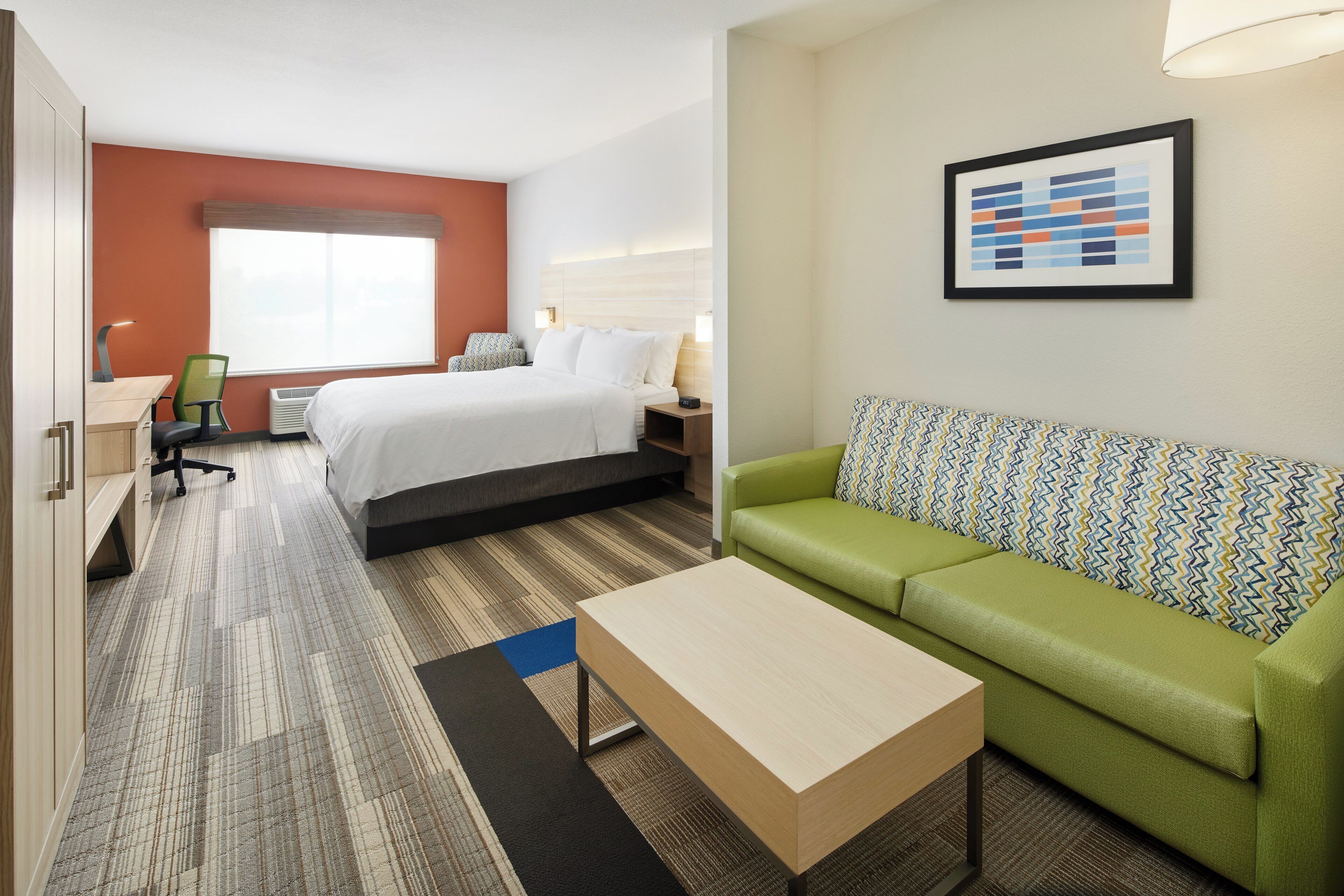 A hotel room with a bed, a desk, a chair, a sofa, a coffee table, and a wall-mounted artwork.