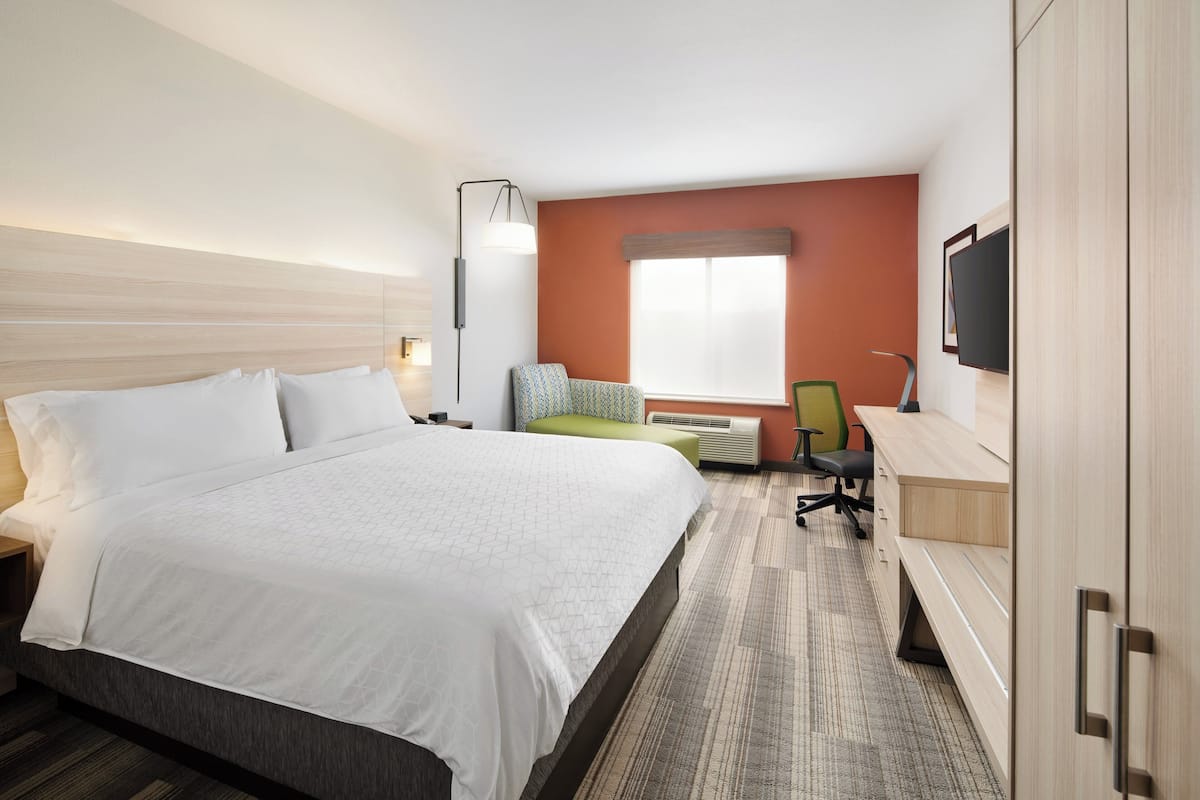 Ett hotellrum med en stor säng, ett skrivbord, en stol, en tv och ett fönster.