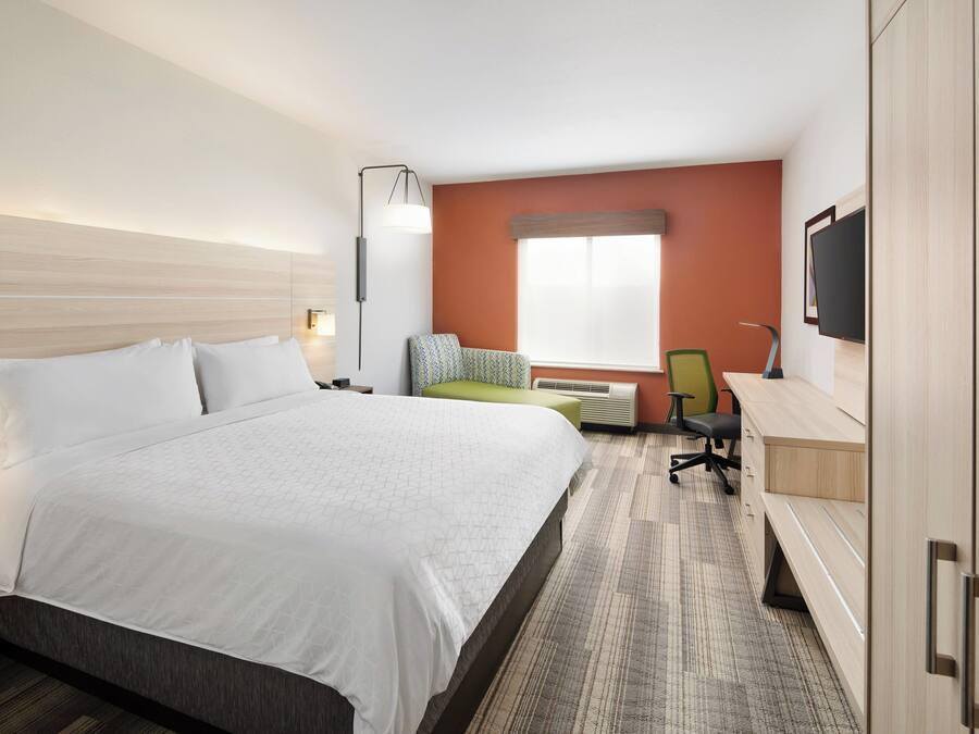 A hotel room with a bed, a desk, a chair, a TV, and a window.