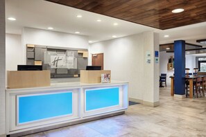 Un espace d’accueil d’hôtel au design moderne, comprenant un comptoir de réception, un réfrigérateur et un panneau indiquant l’emplacement de la réception.
