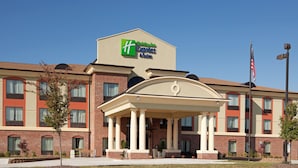 Un hôtel Holiday Inn Express & Suites avec une façade en briques, une entrée centrale dotée d’un porche et un drapeau américain.