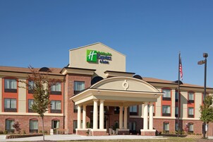 A Holiday Inn Express & Suites hotel with a brick facade, a central entrance with a portico, and an American flag.