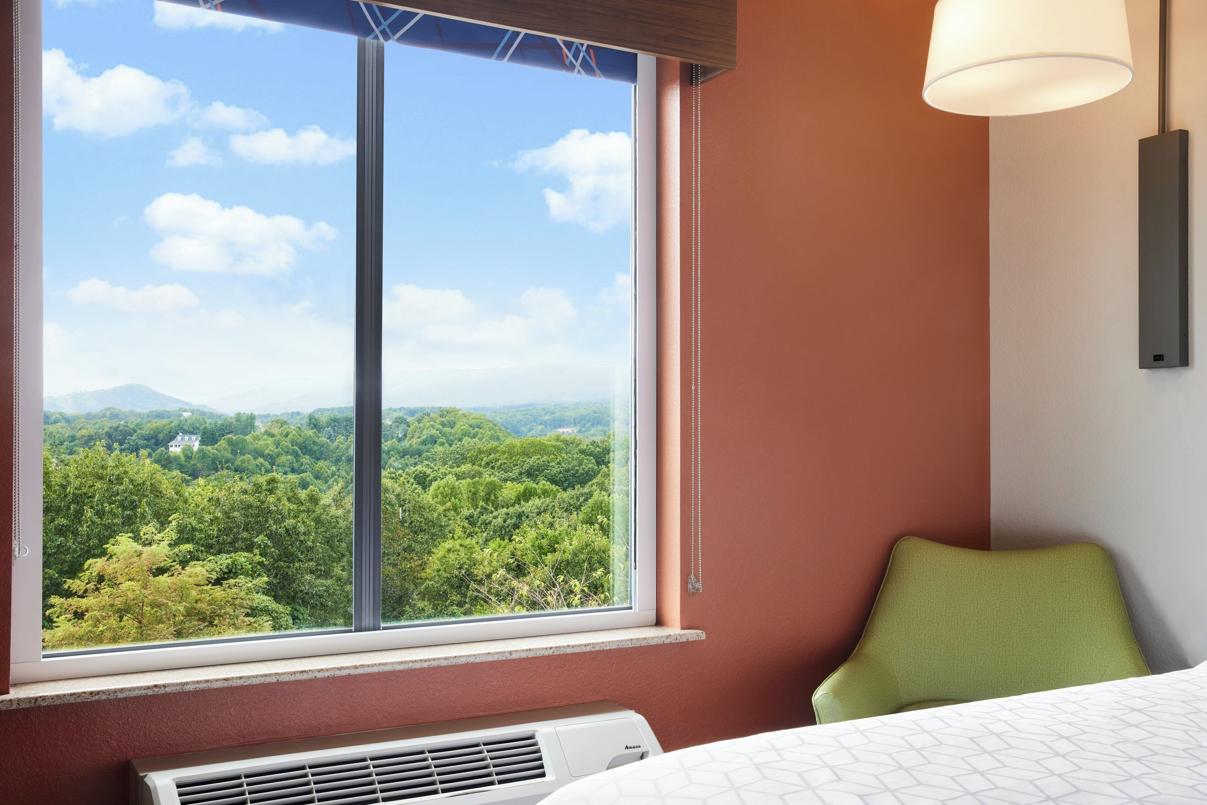 A hotel room with a large window offering a view of a forested landscape.